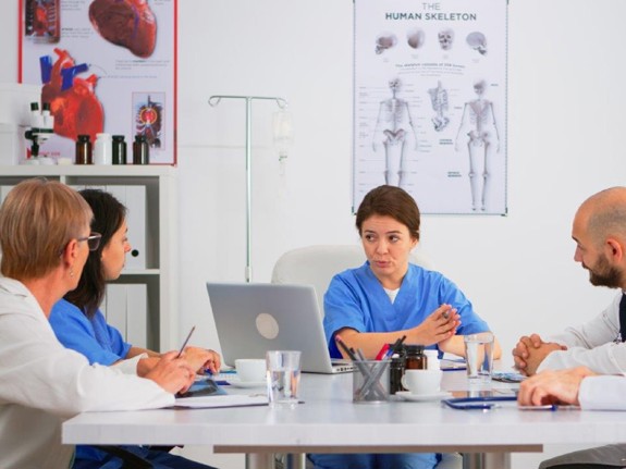 Sjuksköterska som sitter vid ett bord och förklarar något för sina kollegor.