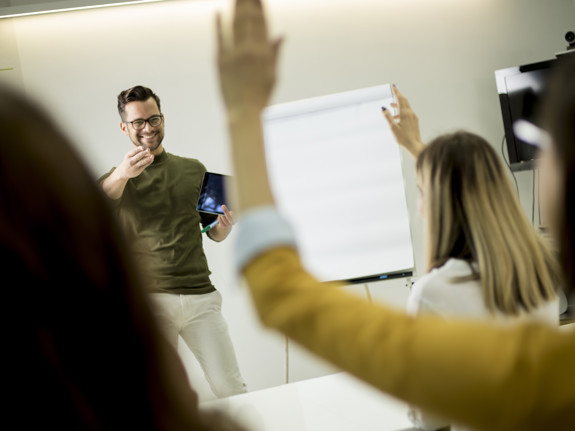 Student som räcker upp handen under en föreläsning. Foto: Mostphotos
