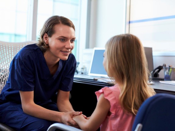 Sjuksköterska sitter och pratar med ett barn.