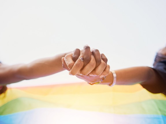 två personer som håller hand framför en regnbågsflagga. Foto: Mostphotos