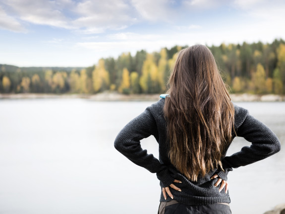 Kvinna som håller händerna på sin rygg vid en sjö. Foto: Mostphotos.