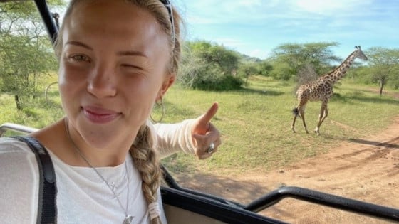 Linnea sitter i en bil och tar en selfie med en giraffe i bakgrunden. Foto: Privat