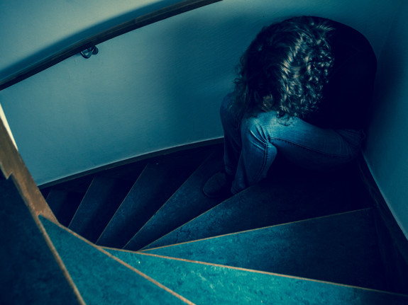 Kvinna som sitter med huvudet nerböjt i en trappa. Foto: Mostphotos