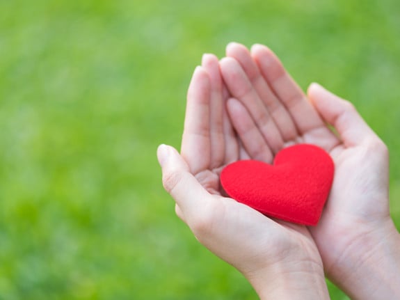 Kvinna som håller ett rött hjärta av tyg i sina händer