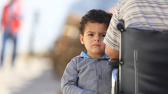 Litet barn som står vid sidan om sin far i rullstol