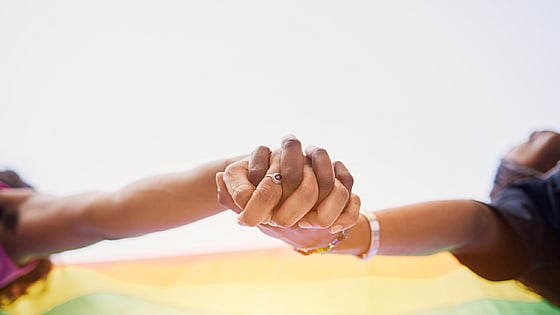 två personer som håller hand framför en regnbågsflagga. Foto: Mostphotos