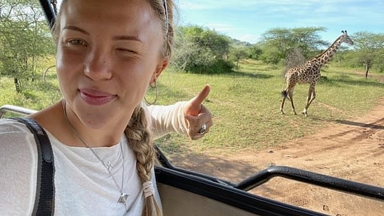 Linnea sitter i en bil och tar en selfie med en giraffe i bakgrunden. Foto: Privat