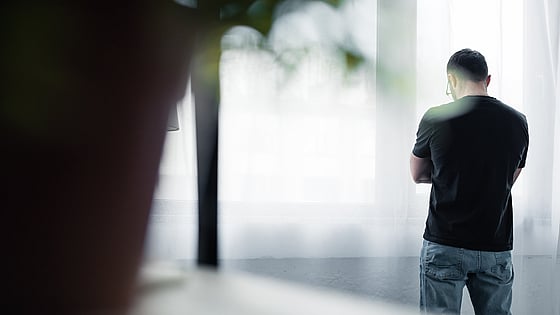 Bild tagen bakifrån på en man som står med armarna i kors vid ett fönster. Foto: Mostphotos