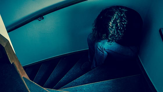 Kvinna som sitter med huvudet nerböjt i en trappa. Foto: Mostphotos