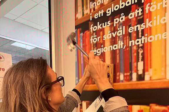 Charlotta Arwidsson spikar sin avhandling på forskningsväggen vid Röda Korsets Högskola. Foto: RKH