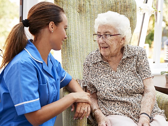 Sjuksköterska som sitter med en äldre dam. Foto:Mostphotos