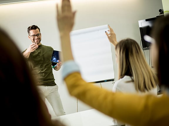 Student som räcker upp handen under en föreläsning. Foto: Mostphotos
