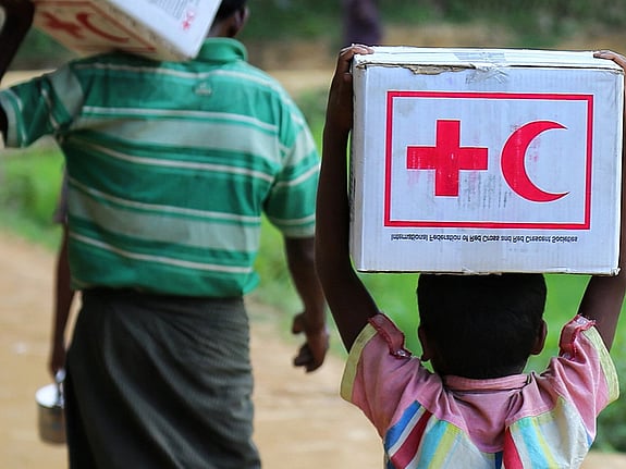 Barn som går med en kartonglåda med Röda Korsets/Röda Halvmånens logga på. Foto: Mostphotos