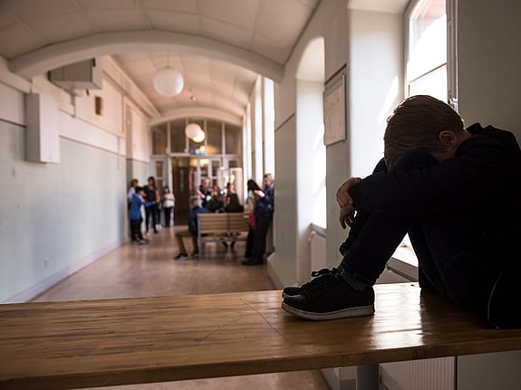 Elev som sitter med huvudet mellan benen i en skolkatalog. Foto: Mostphotos