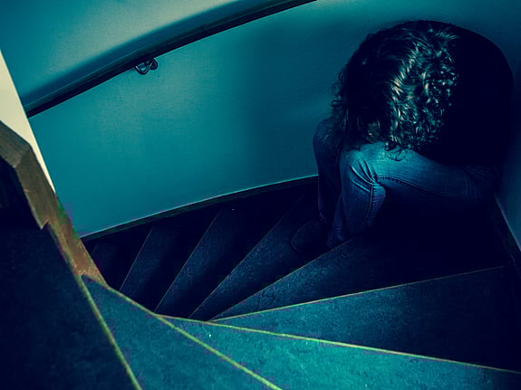 Kvinna som sitter med huvudet nerböjt i en trappa. Foto: Mostphotos