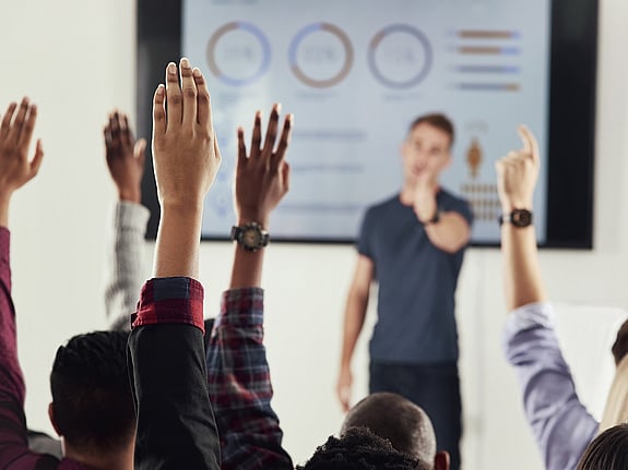 Studenter som räcker upp händerna under en föreläsning. Foto: Mostphotos