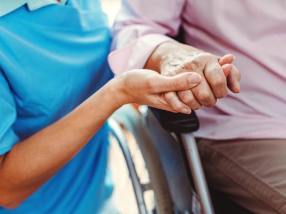 Sjuksköterska håller en äldre kvinna i handen.