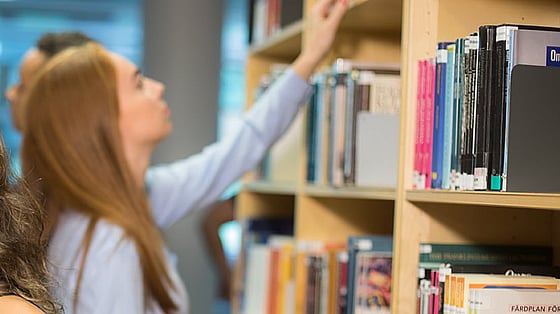 Kvinna som letar efter böcker i bibliotek. Foto: Mostphotos