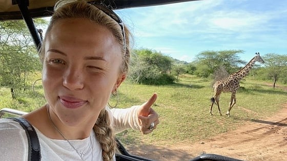 Linnea sitter i en bil och tar en selfie med en giraffe i bakgrunden. Foto: Privat