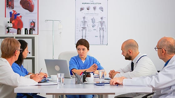 Sjuksköterska som sitter vid ett bord och förklarar något för sina kollegor.